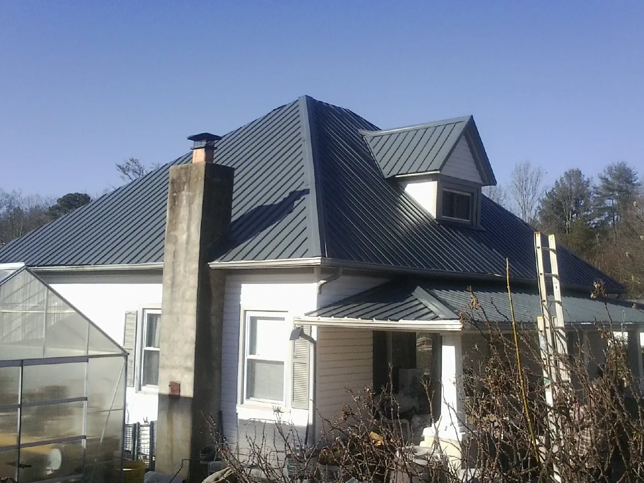 Dark blue standing seam metal roof on a white farmhouse with dormer — Slate & Tile Roof Repair by Roofing Brothers in Forest Hills
