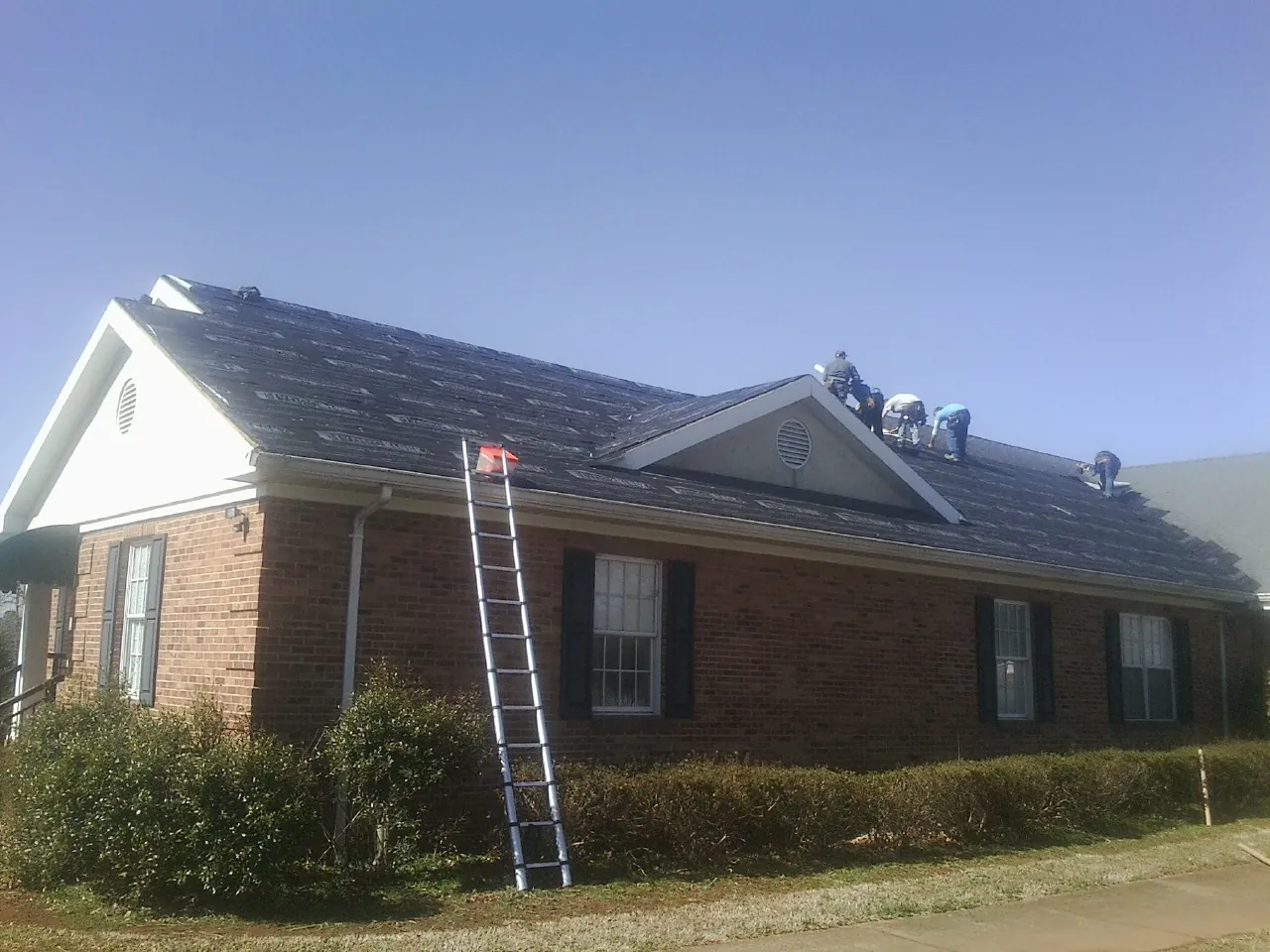Crew tearing shingles off a brick ranch roof with a ladder set — Metal Roof Repair work by our crew in Forest Hills