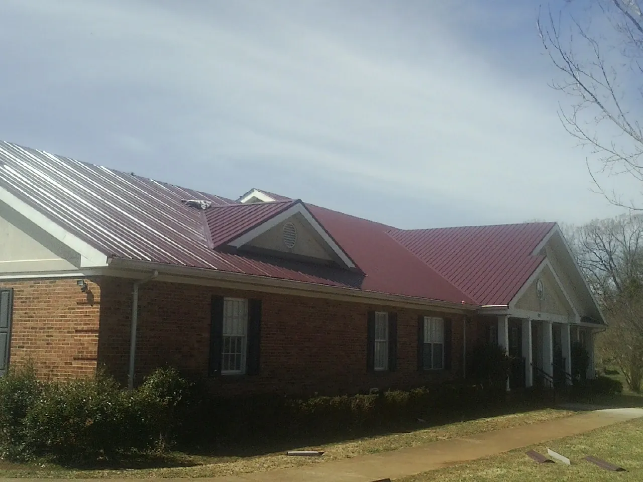 Red metal roof with gabled entries on a long brick building, from a Hail Damage Roof Repair job in Forest Hills