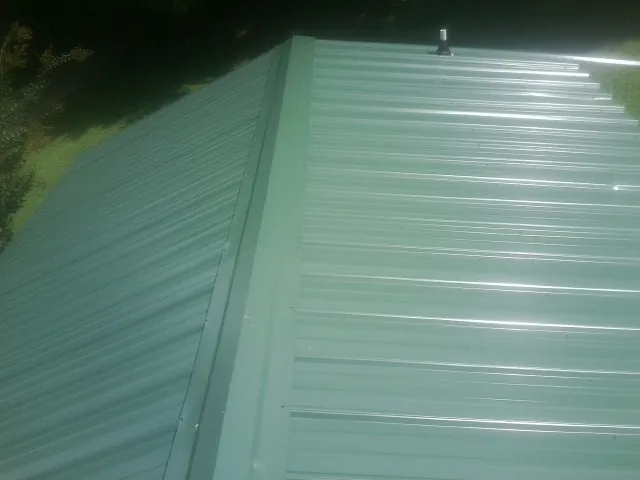 New green metal panels meeting at the ridge of a roof — Flat Roof Repair work by our crew in Forest Hills