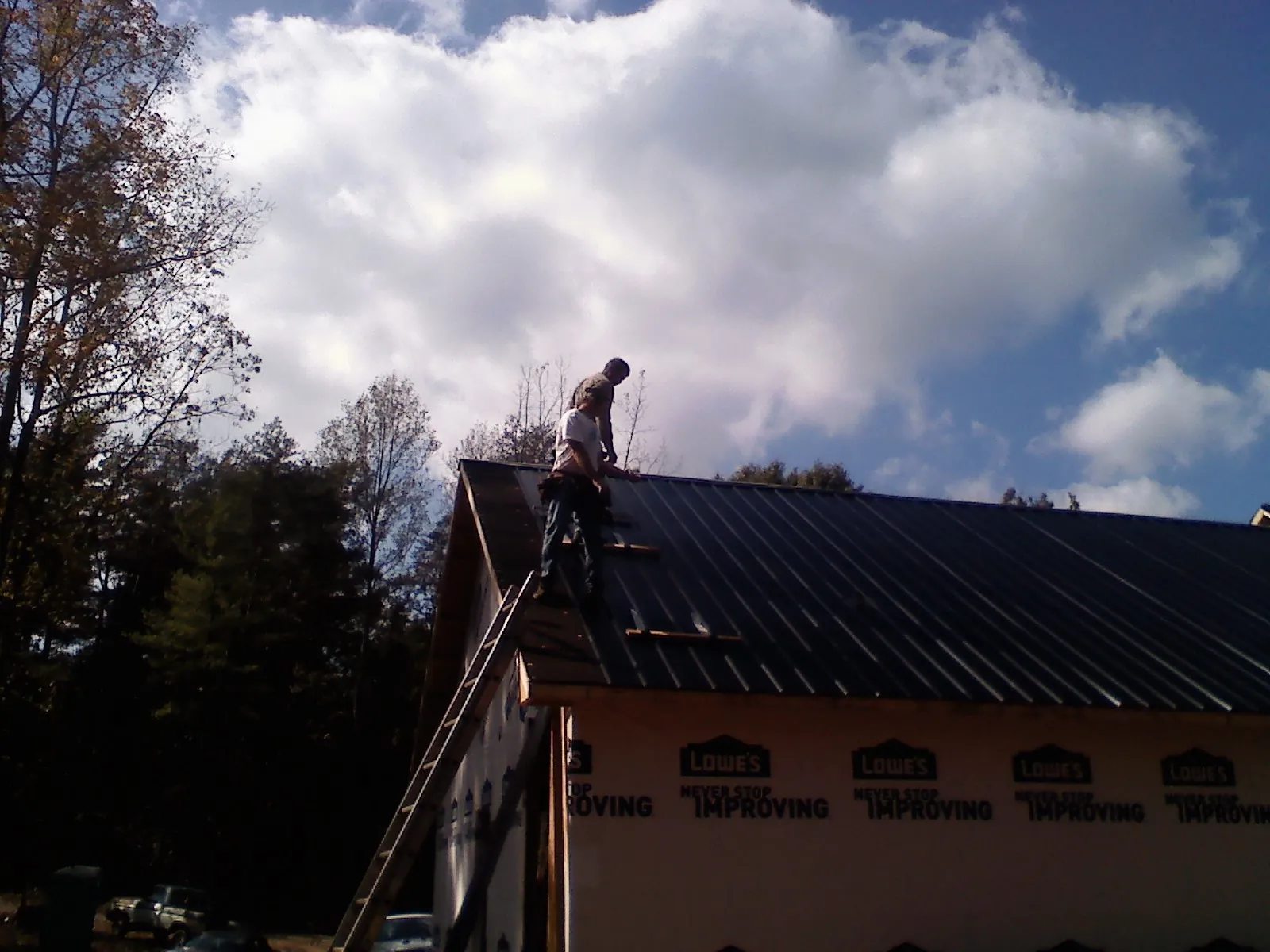 Roofer fastening dark metal panels high against a cloudy sky, from a Roof Inspection job in Forest Hills
