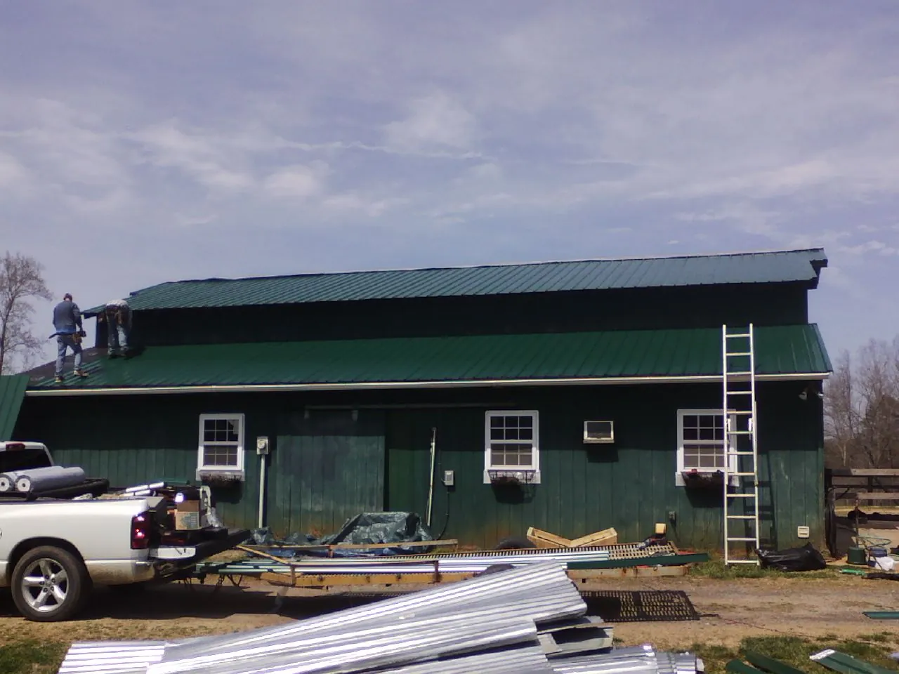 Crew installing green metal roofing on a large green barn in Forest Hills