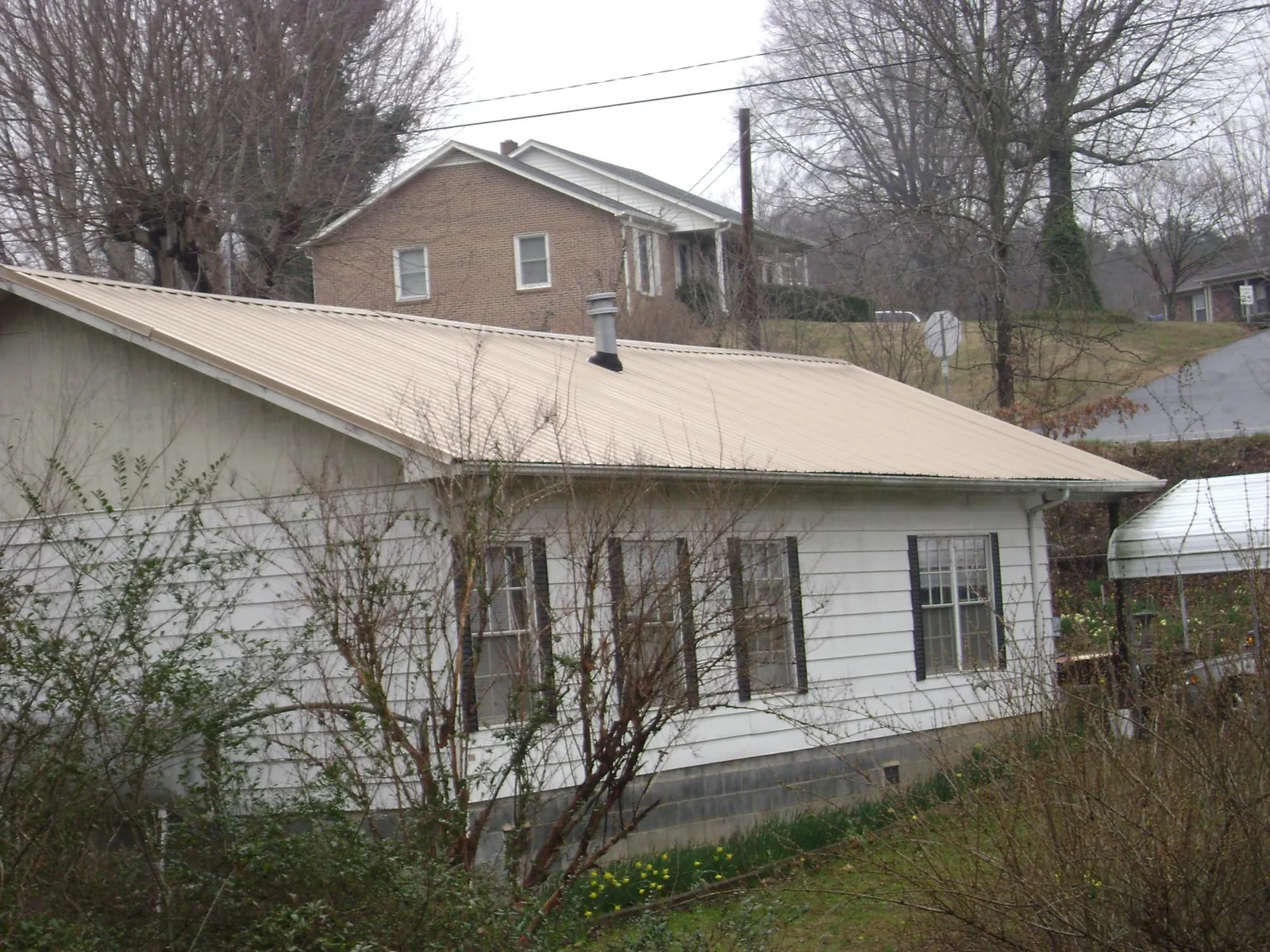 Tan metal roof on a white sided house set into a hillside — Commercial Roofing by Roofing Brothers in Forest Hills