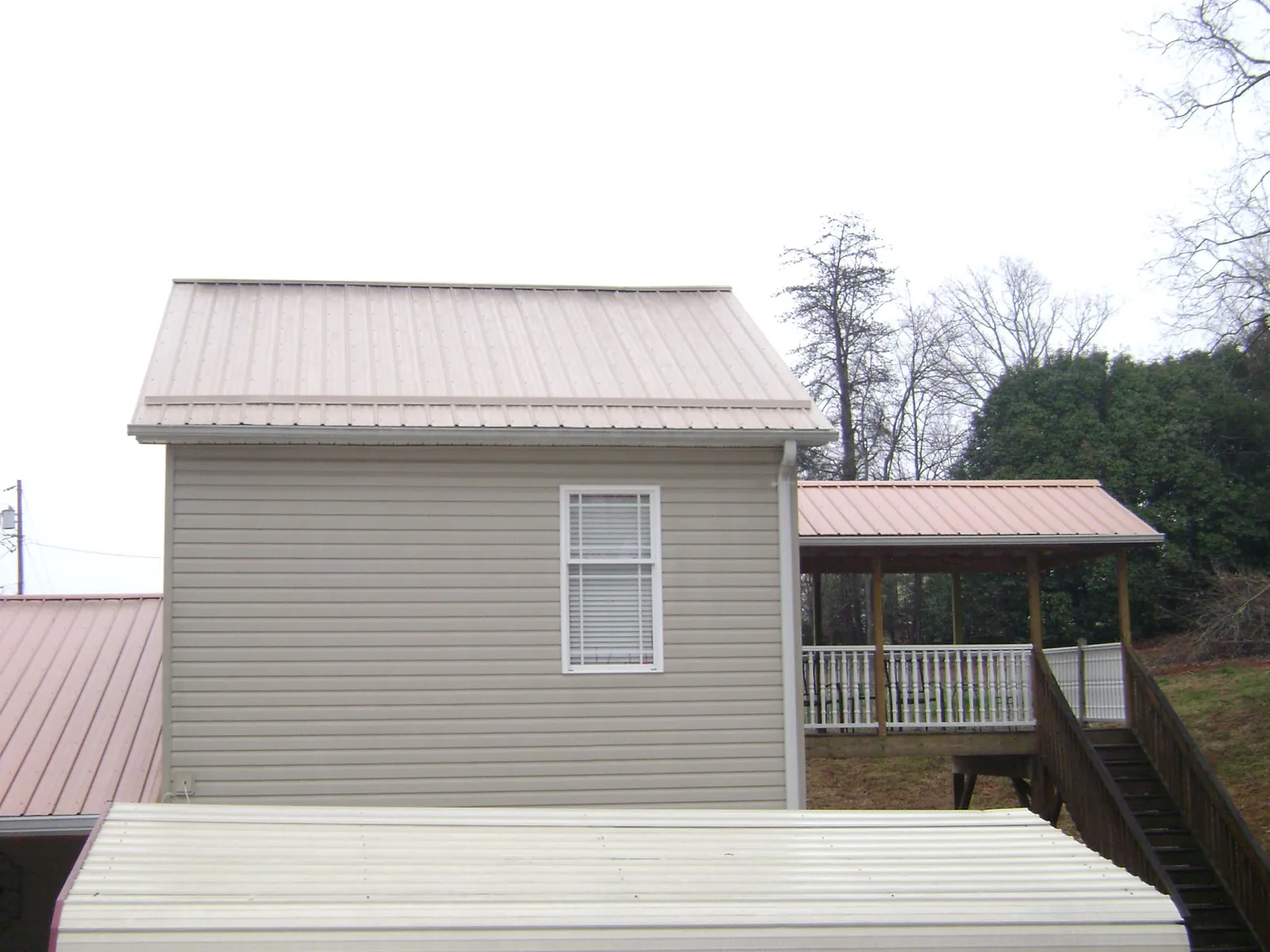Tan metal roofs on a two story addition and attached porch, from a Roof Replacement job in Forest Hills